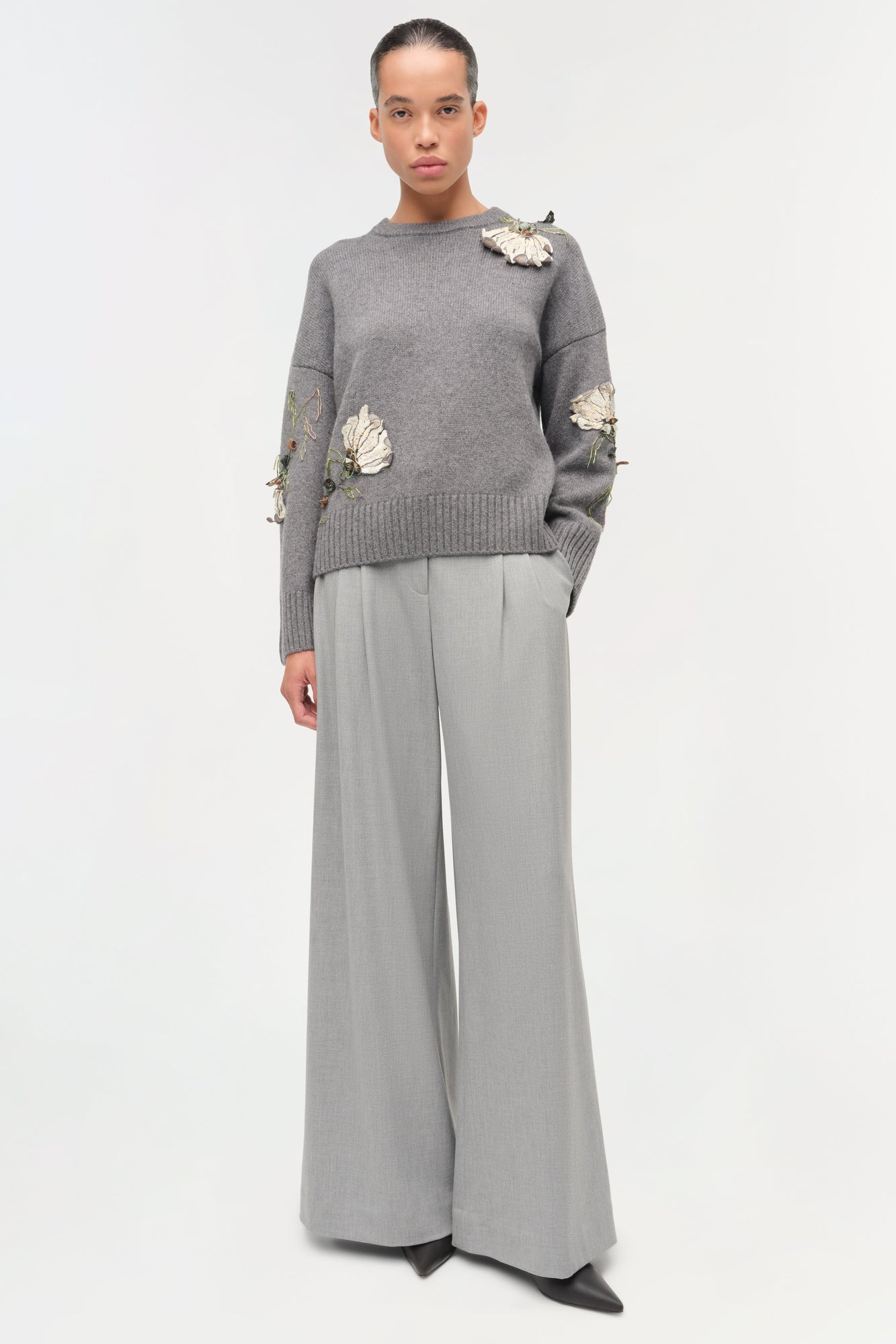 Gray knit sweater with cream floral embellishments on shoulders and sleeves, paired with gray wide-leg trousers.
