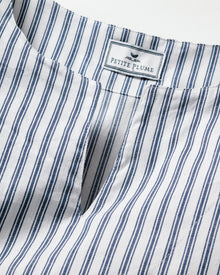 Close-up of a breathable cotton fabric with vertical navy blue and white stripes, featuring a notch neckline. A label at the back reads Petite Plume with a bird logo. Ideal for luxurious sleepwear or stylish caftans, this is the Girls Twill Caftan in Navy French Ticking by Petite Plume.