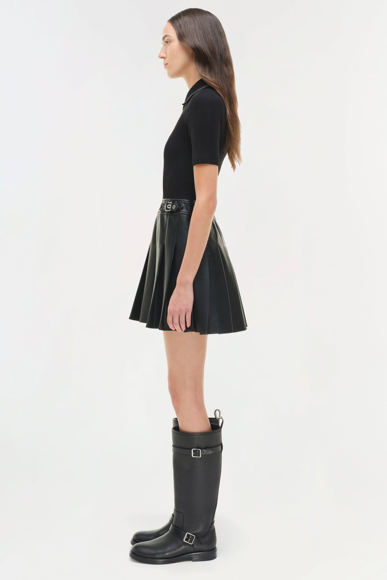 Woman wearing black ribbed knit short-sleeve top with pleated leather skirt and black buckled knee-high boots.