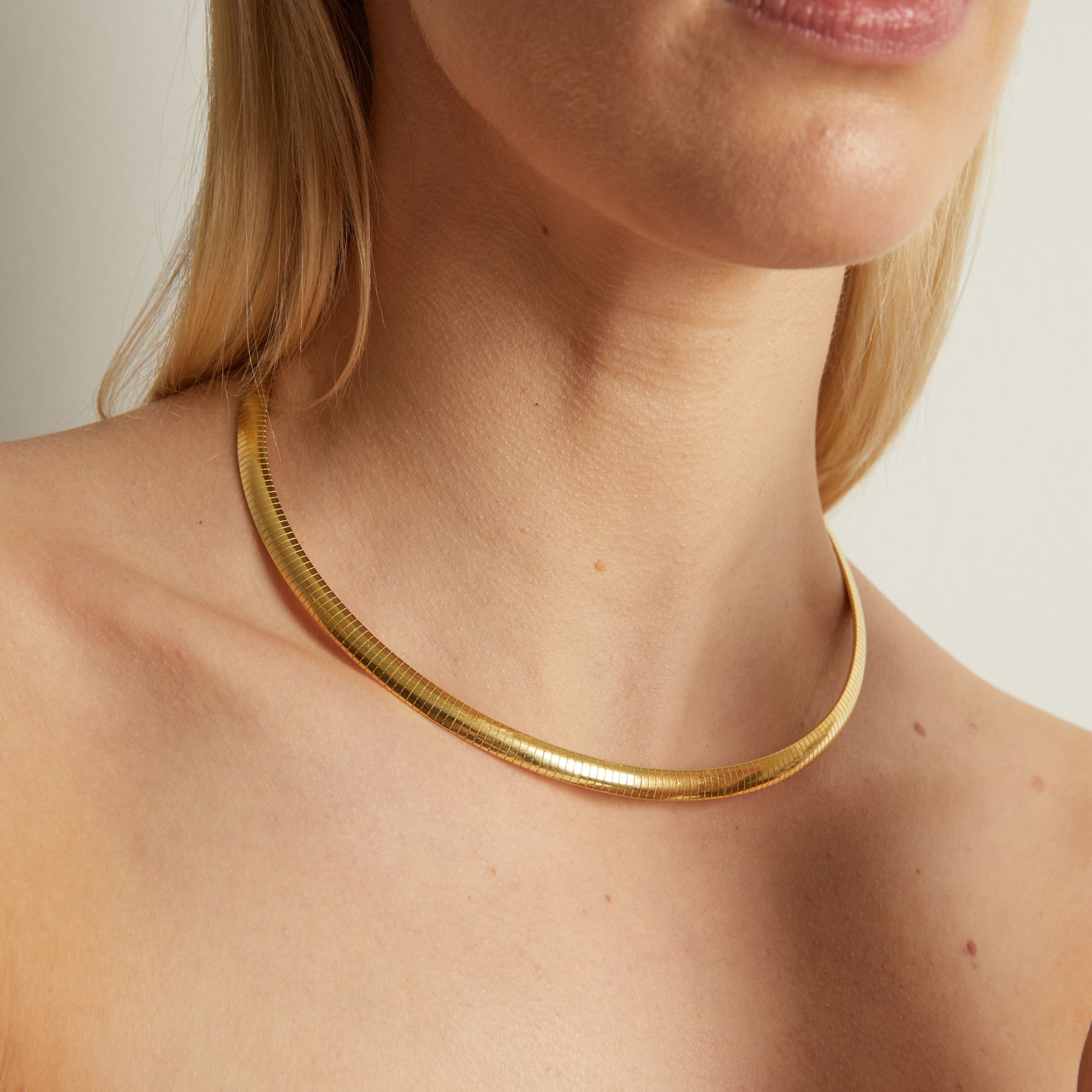 Gold necklace worn by a person on a neutral background