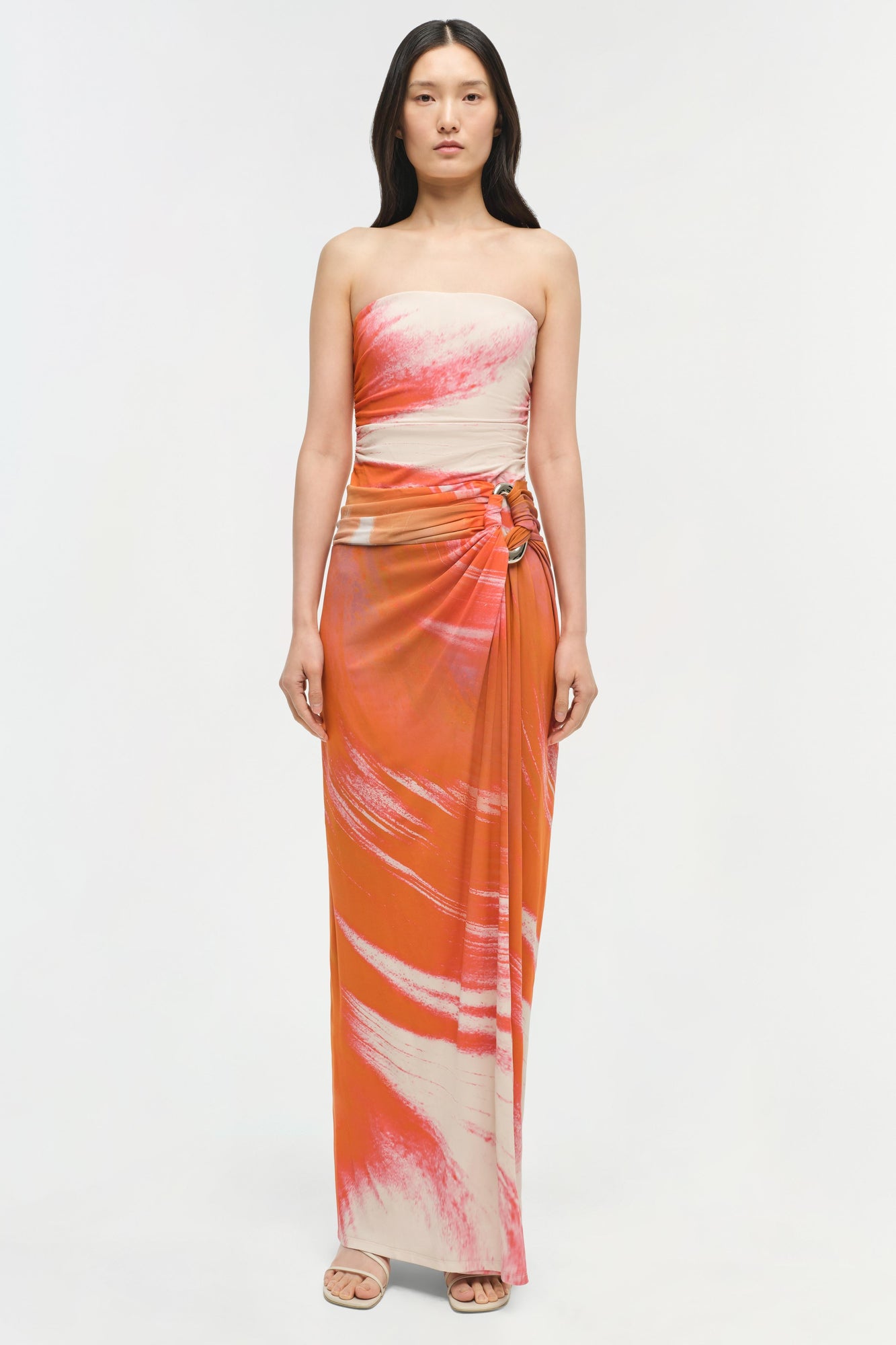 Woman wearing strapless jersey gown with cream, coral, and orange watercolor pattern and ruched waist detail.