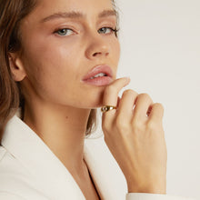 Model. Close-up of a woman wearing a gold ring on a plain background