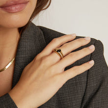 Model. Close-up of a hand wearing a gold ring with a black stone, holding a textured gray fabric.