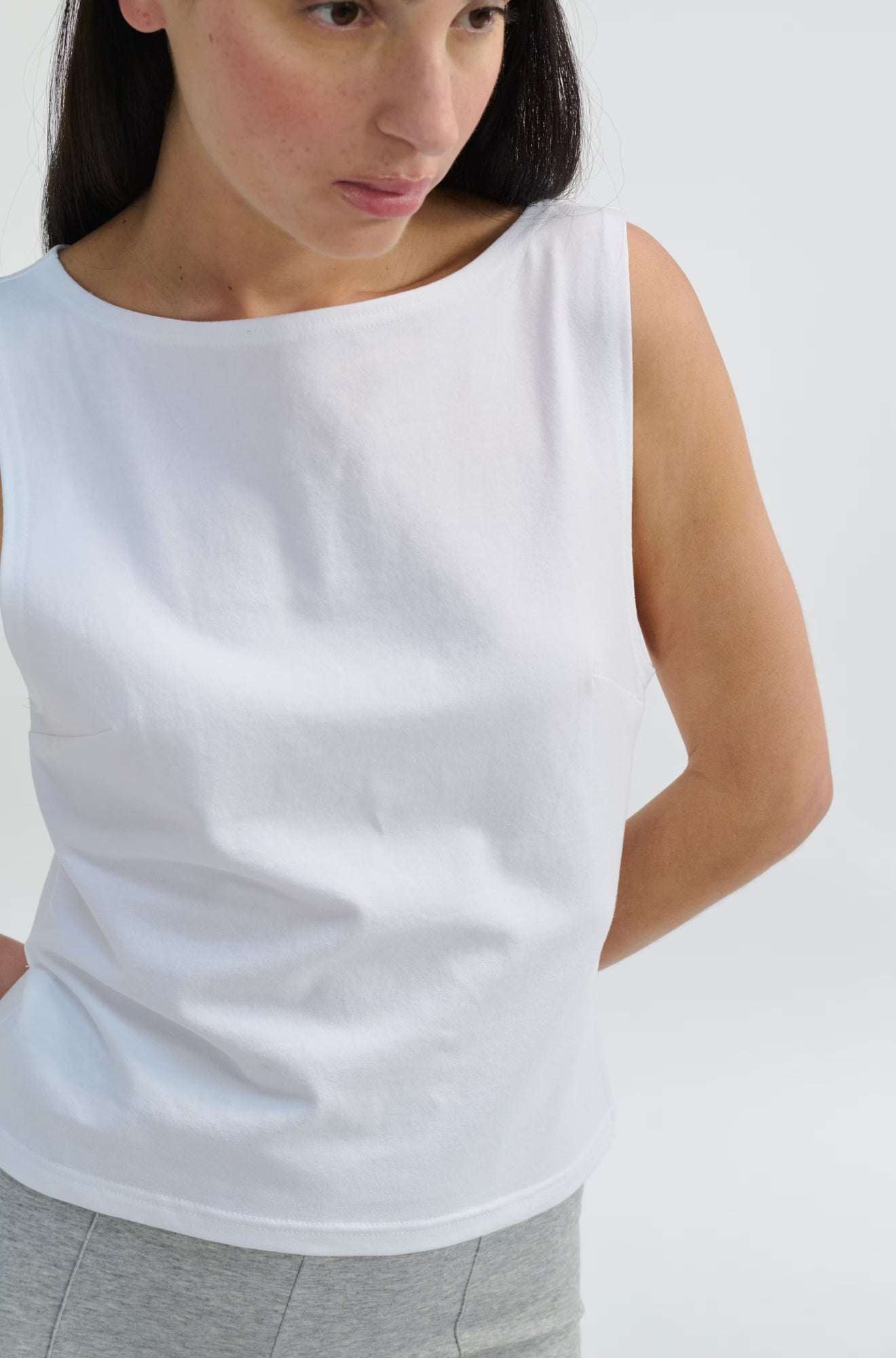 Woman wearing a white sleeveless top against a plain background