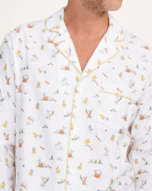 A man with short gray hair wears the Men's Twill Pajama Set in Easter Frolic—white pants and a long-sleeve top with a small, colorful print—standing barefoot against a plain light background.