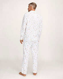 A man with short gray hair wears the Men's Twill Pajama Set in Easter Frolic—white pants and a long-sleeve top with a small, colorful print—standing barefoot against a plain light background.