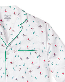 The Mens Flannel Pajama Set in Apres Ski by Petite Plume, crafted from 100% cotton, features small skiers in red and blue amidst tiny green trees. It includes a white top with a front pocket, green piping, and white buttons.