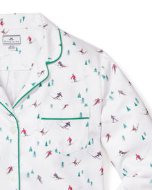 The Womens Flannel Pajama Set in Apres Ski by Petite Plume is a white brushed cotton flannel top featuring a vibrant skier and pine tree pattern, accented with green piping on the collar and pocket for stylish comfort.