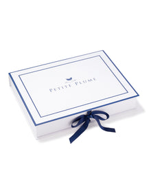A white rectangular box, blue-edged, displays Petite Plume with a bird graphic above. Tied with a dark blue ribbon, it echoes the elegance of Womens Gauze Willow Scoopneck Top in Pink from Petite Plumes luxury Gauze Collection.