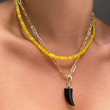 Shimmering beaded necklace made of smooth opals in shades of yellow on a gold linking ovals clasp
Styled on a neck layered with a paperclip chain with a Black Horn Charm dangling