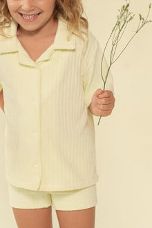 Child wearing buttercream ribbed short-sleeve button-up shirt and matching mini bike shorts.