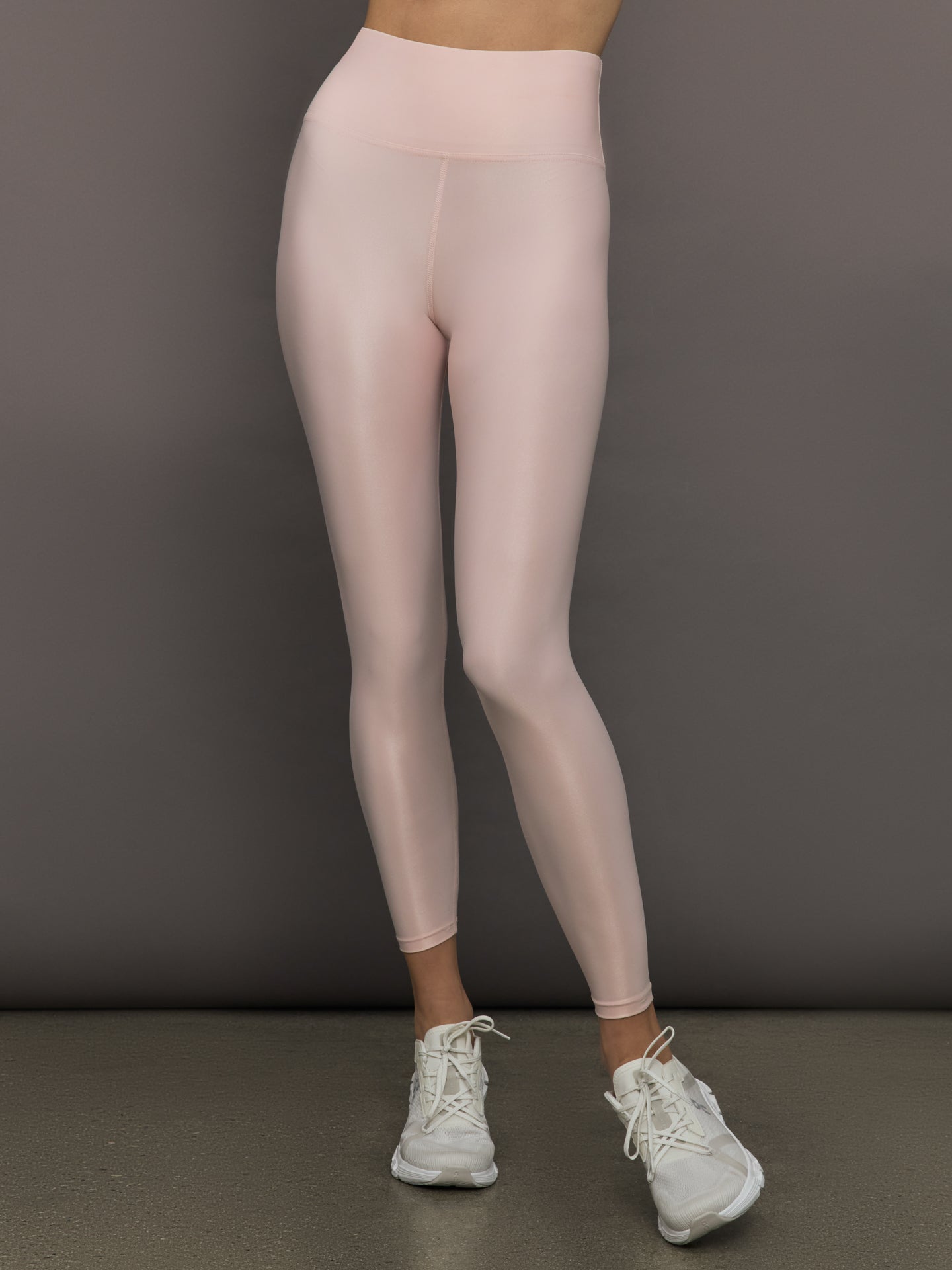 Model wears a pair of high rise baby pink sleek liquidy shine leggings. 