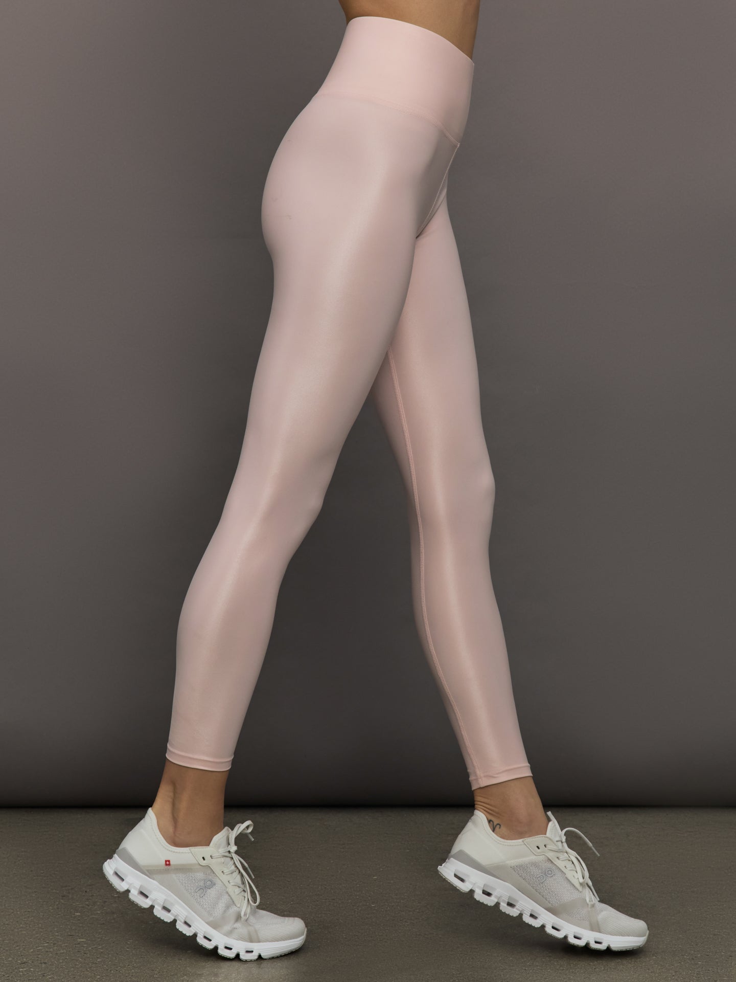 Model wears a pair of high rise baby pink sleek liquidy shine leggings. 