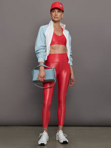 Model wears a high rise pair of bright red leggings with a liquidy shine finish. 