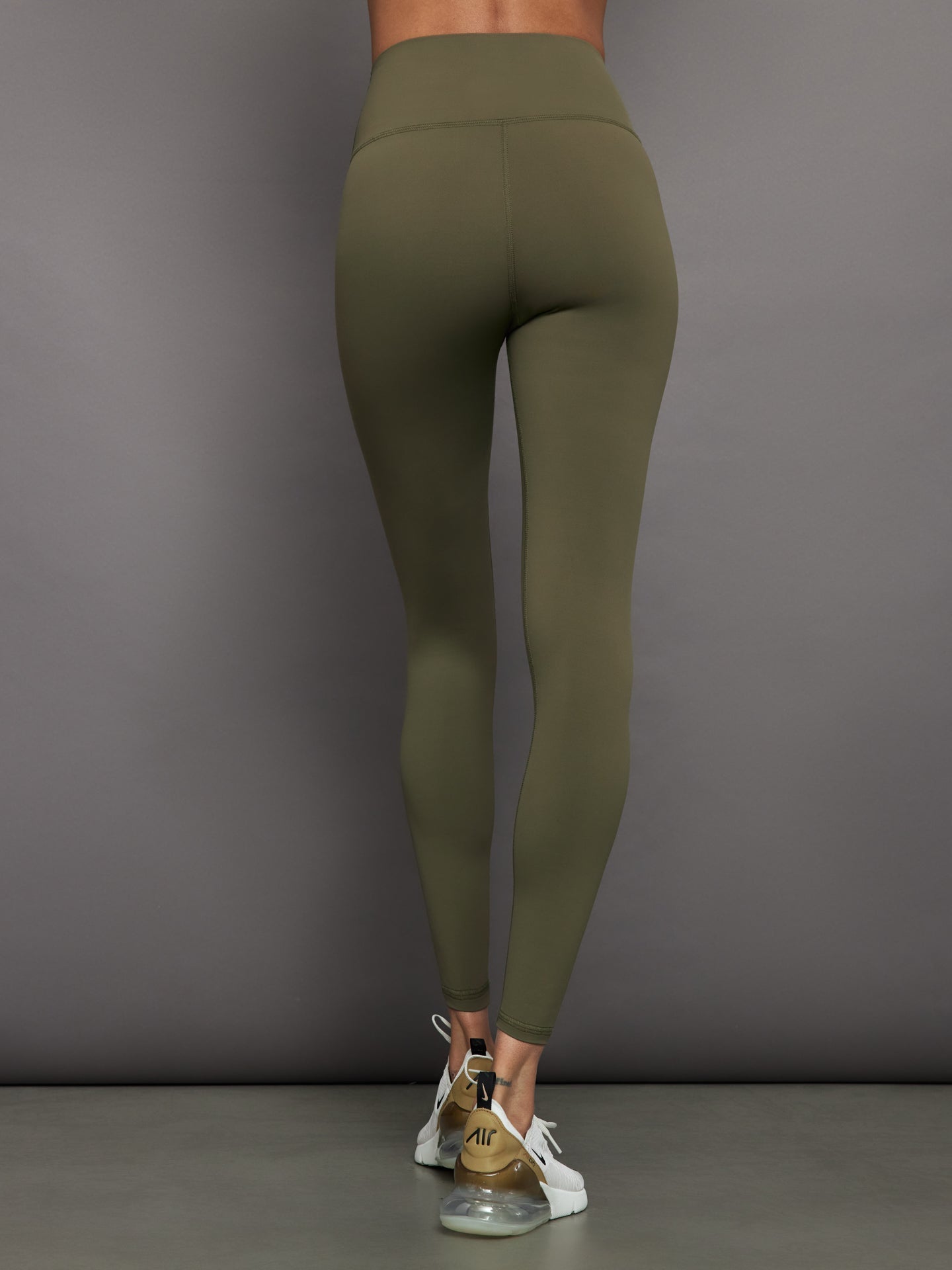 Model wears full-length olive leggings with a high-rise wide waistband and smooth, compressive fabric.