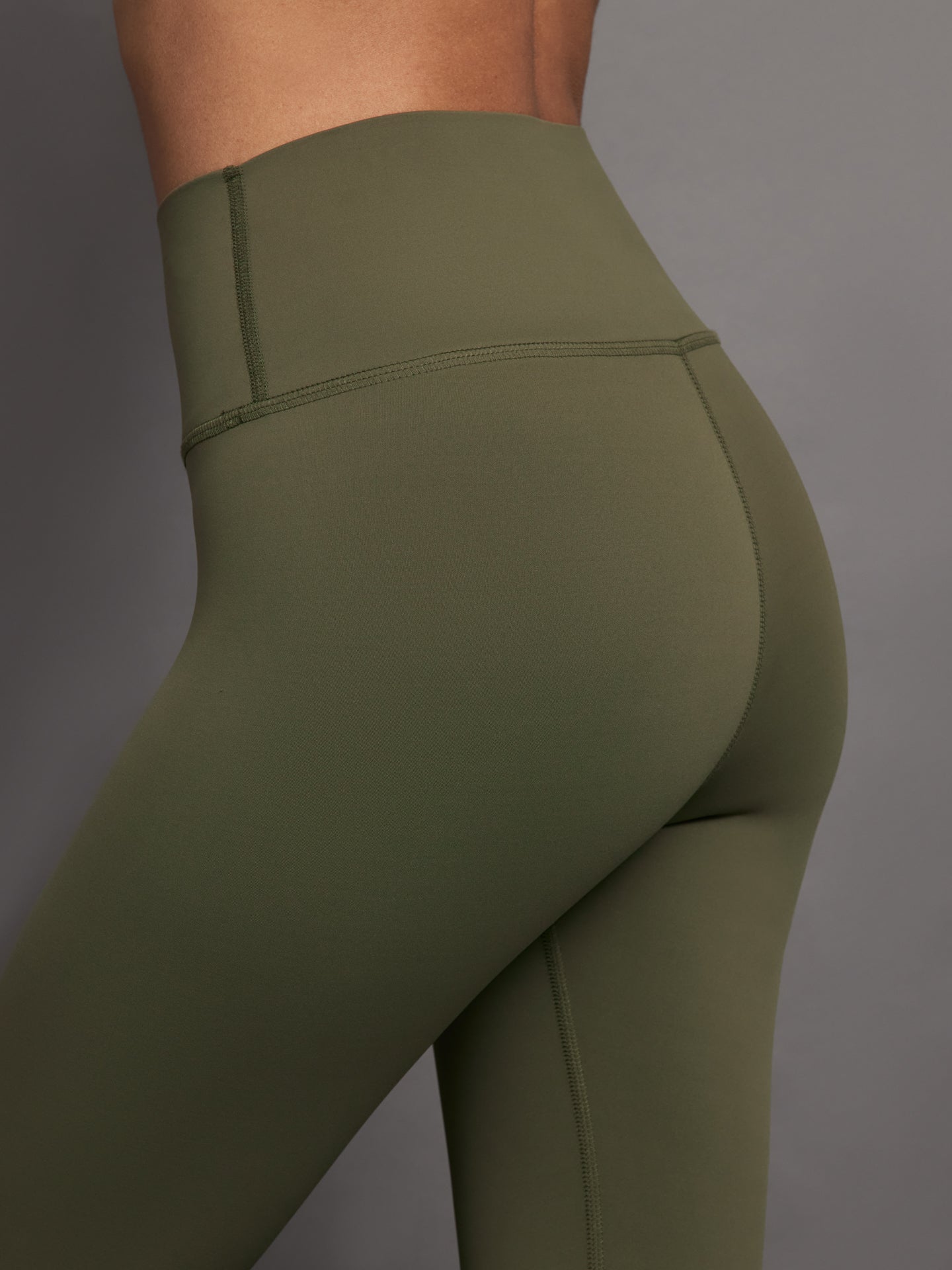 Model wears full-length olive leggings with a high-rise wide waistband and smooth, compressive fabric.