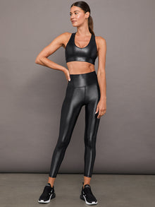 Model wears a high waisted pair of liquidy shine black leggings that hit at model's ankle.