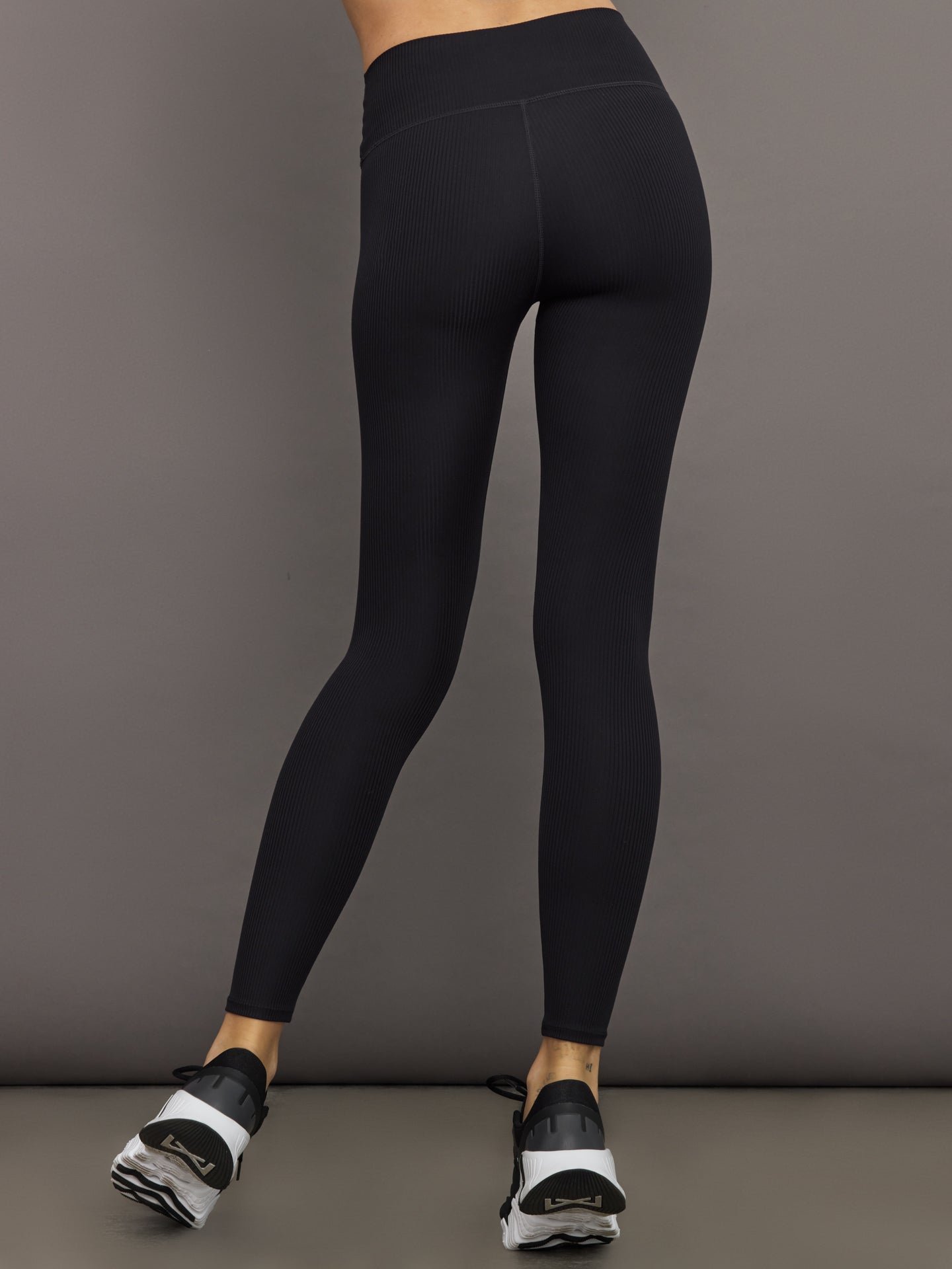 Model wears black high-rise leggings with a ribbed texture and a smooth, body-hugging fit.
