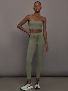 Model wears a buttery soft sports bra in army green with double straps and cross back design. 