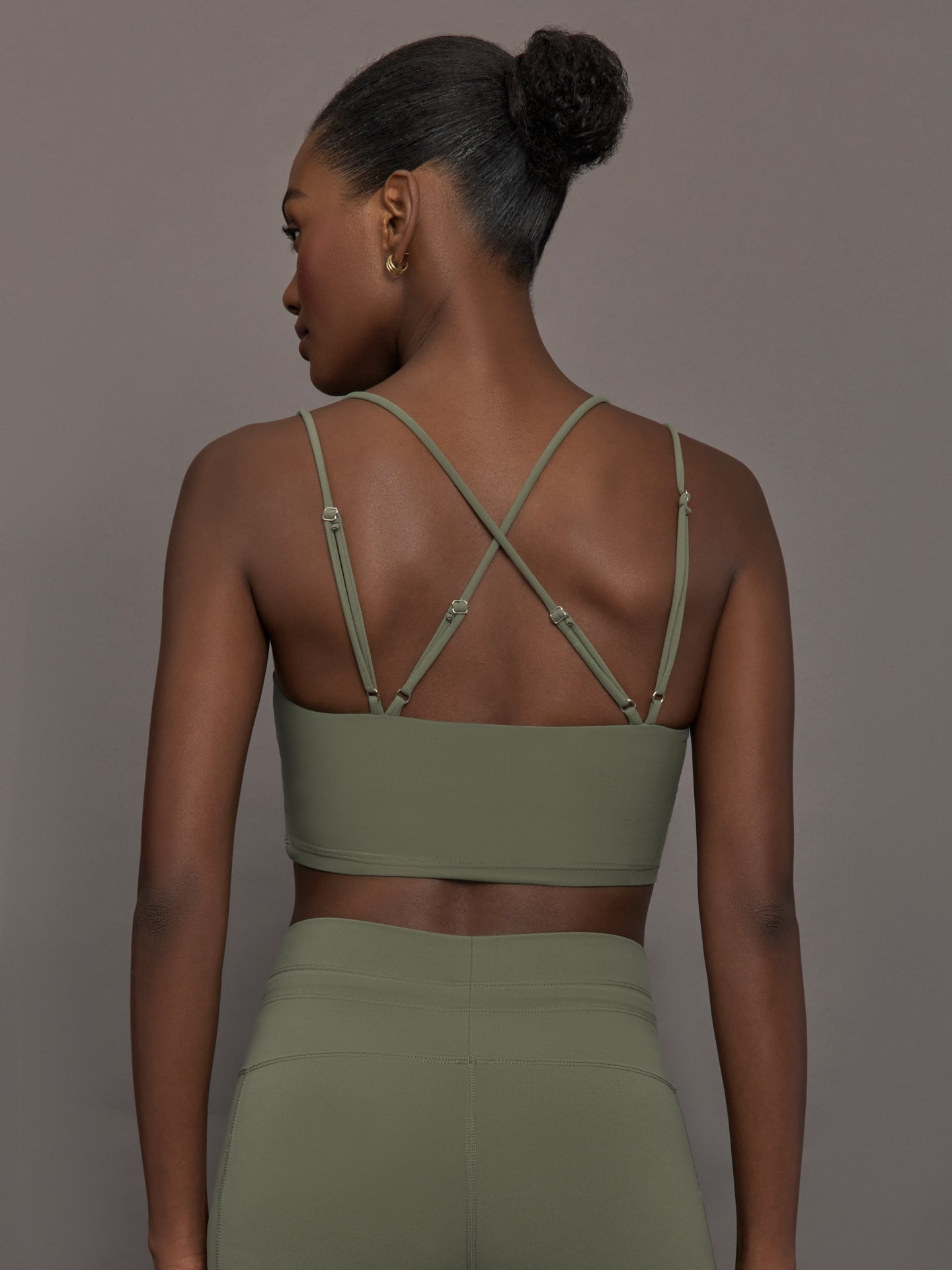 Model wears a buttery soft sports bra in army green with double straps and cross back design. 