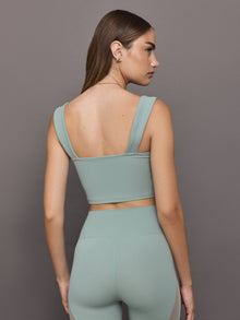 Model wears sage green bra top with a square neckline and wide shoulder straps.