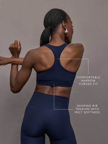 Model stretching in ribbed Melt racerback bra in true navy, back angled view.