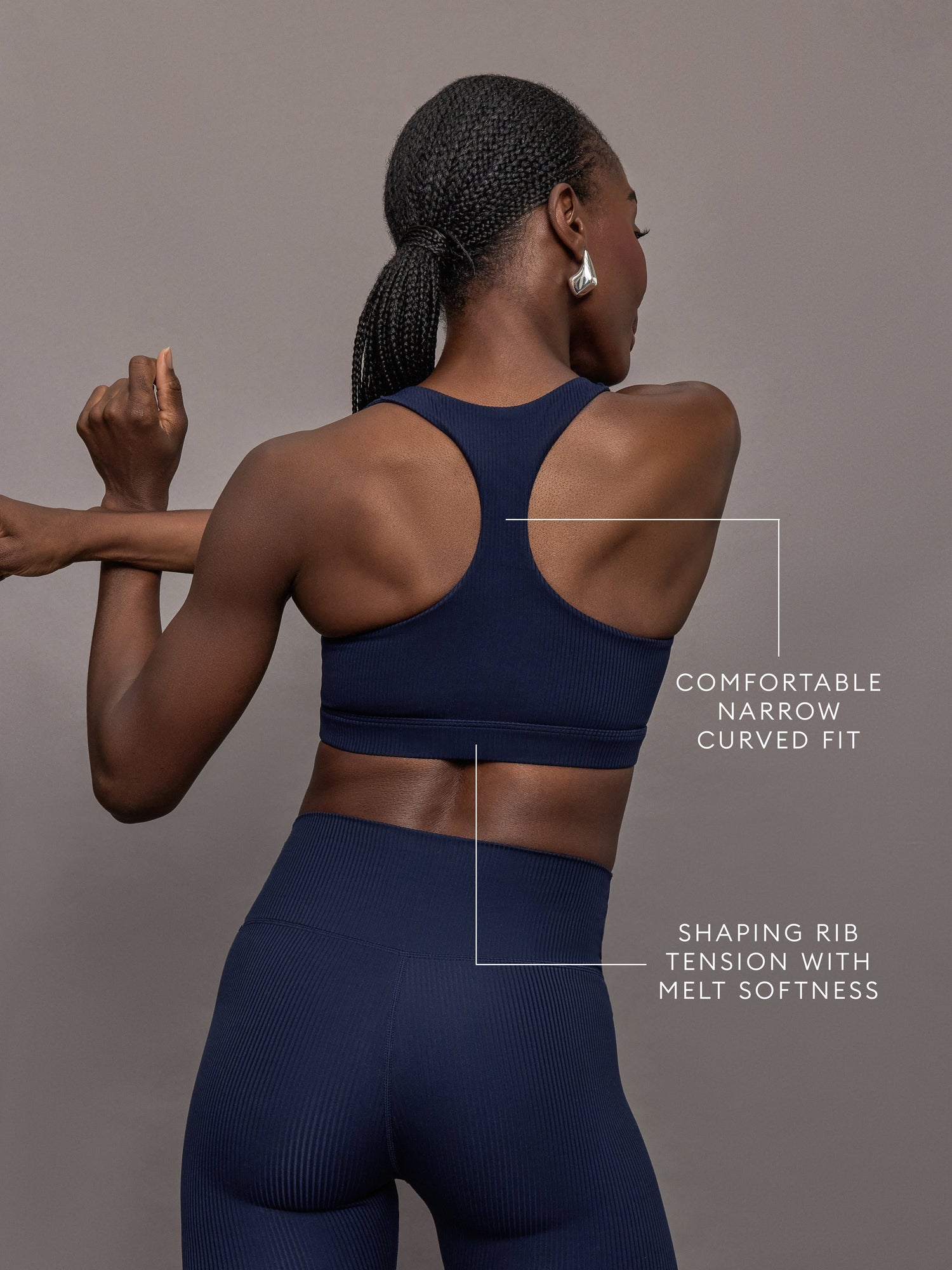Model stretching in ribbed Melt racerback bra in true navy, back angled view.