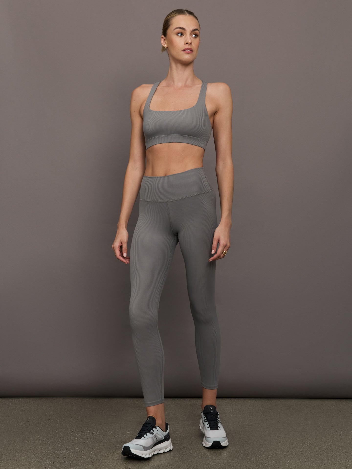 Model wears steel grey-colored racerback bra with a ribbed texture, square neckline, and wide straps that merge at the back.
