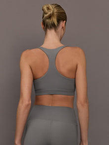 Model wears steel grey-colored racerback bra with a ribbed texture, square neckline, and wide straps that merge at the back.
