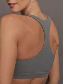 Model wears steel grey-colored racerback bra with a ribbed texture, square neckline, and wide straps that merge at the back.
