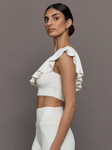 Model wears a white one shoulder sports bra with a ruffled overlay. 