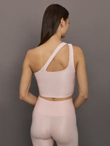 Model wears shiny, asymmetrical one-shoulder bra top in light pink, with a smooth, reflective fabric.