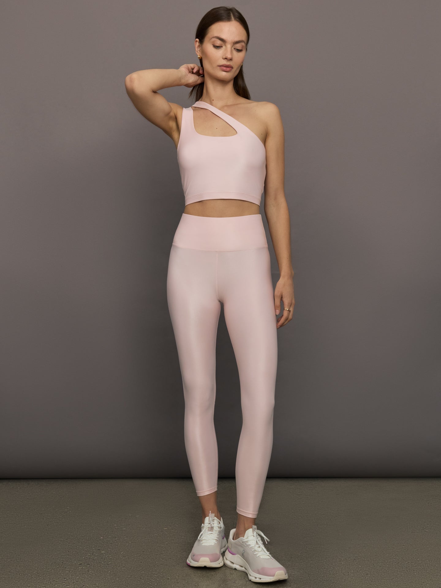 Model wears shiny, asymmetrical one-shoulder bra top in light pink, with a smooth, reflective fabric.