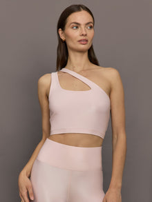 Model wears shiny, asymmetrical one-shoulder bra top in light pink, with a smooth, reflective fabric.