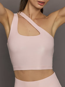 Model wears shiny, asymmetrical one-shoulder bra top in light pink, with a smooth, reflective fabric.