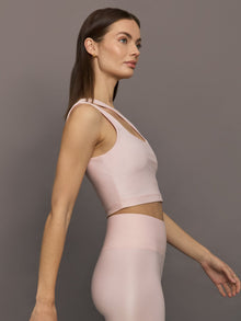 Model wears shiny, asymmetrical one-shoulder bra top in light pink, with a smooth, reflective fabric.