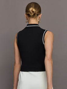 Model wears a sleeveless black tennis polo with three white buttons. 