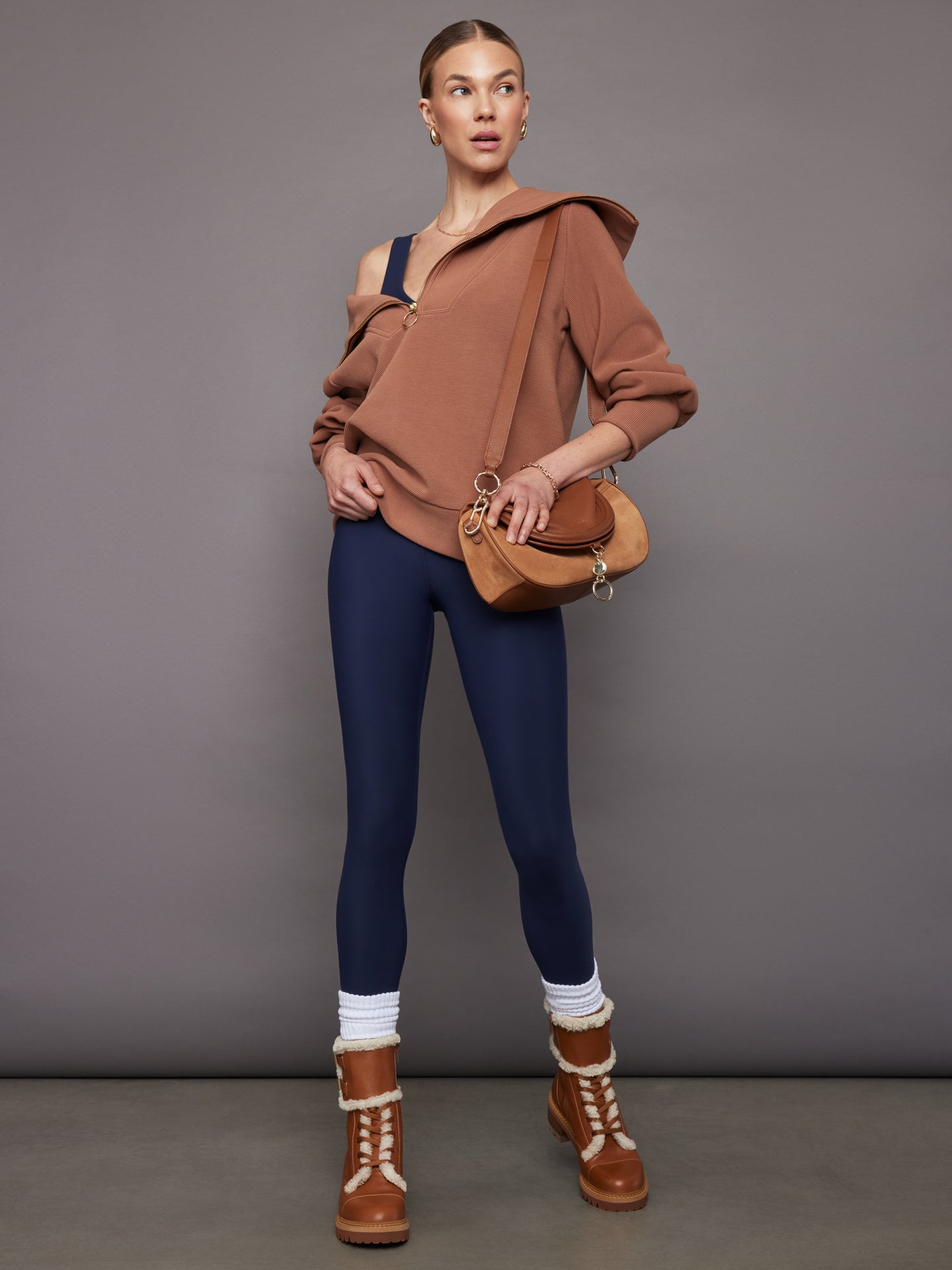 Styled outfit: navy jumpsuit layered with brown zip sweater, boots, and bag.