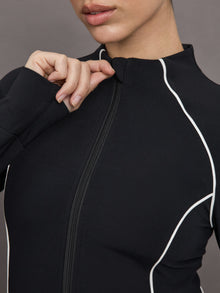 Model wears a black mock neck long sleeve top with thumb holes with thin white stripes outlining a corseted physique.