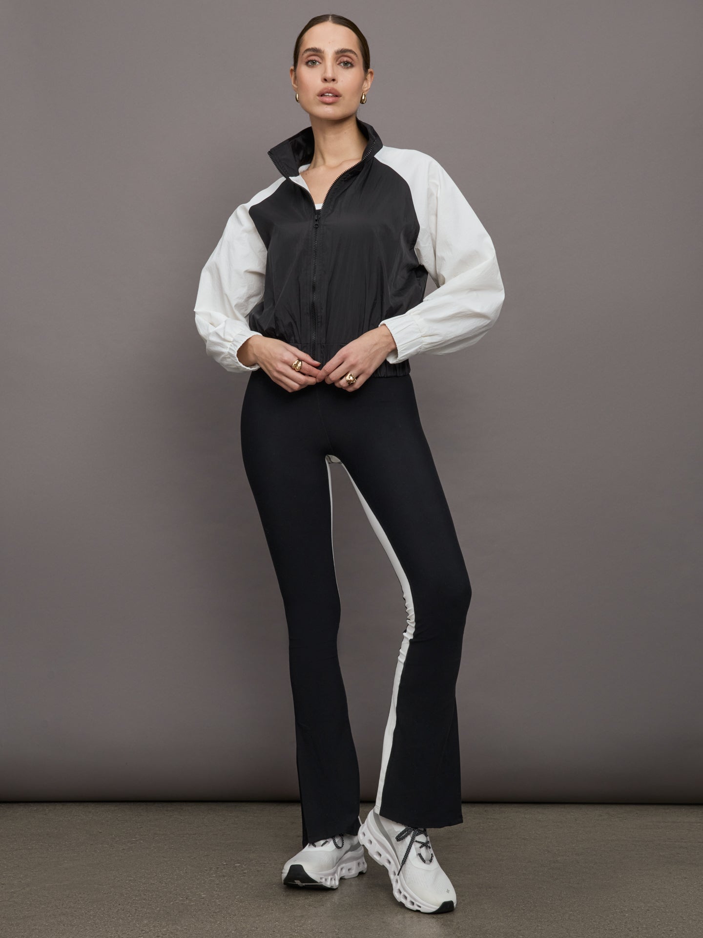 Model wears a cropped windbreaker with a popped collar, black bodice and white long sleeves with a cinched wristline.