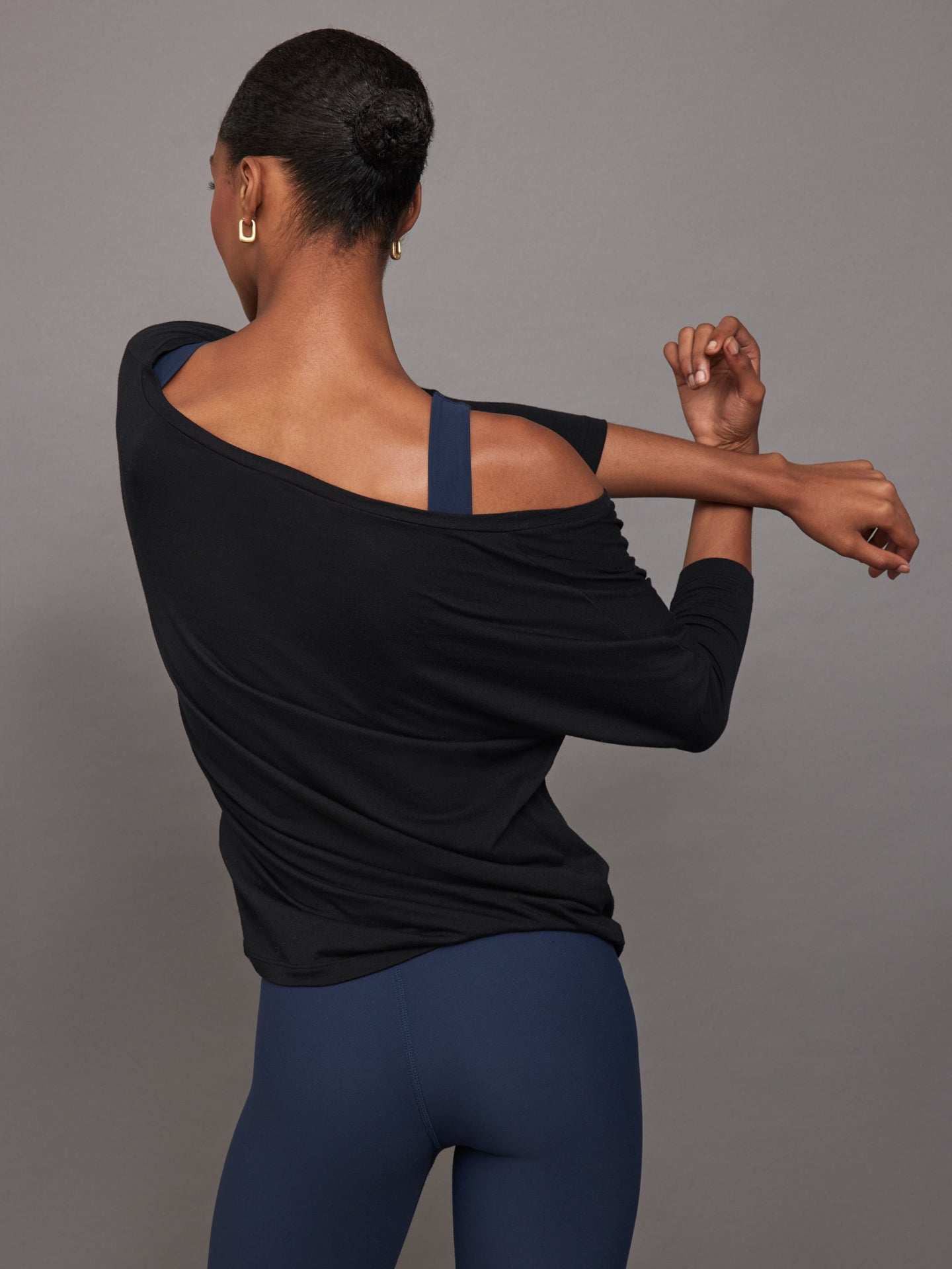Three quarter back view of model in Long Sleeve Off Shoulder Tee Black with off shoulder detail.
