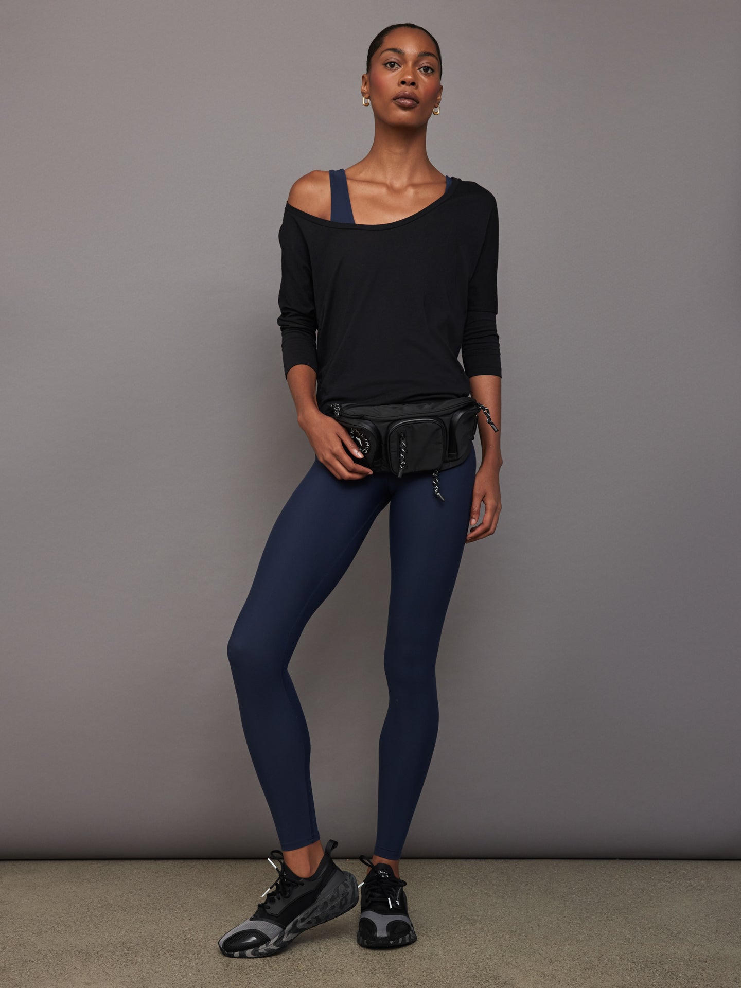 Full body view of model styled in Long Sleeve Off Shoulder Tee Black with navy leggings and sneakers.