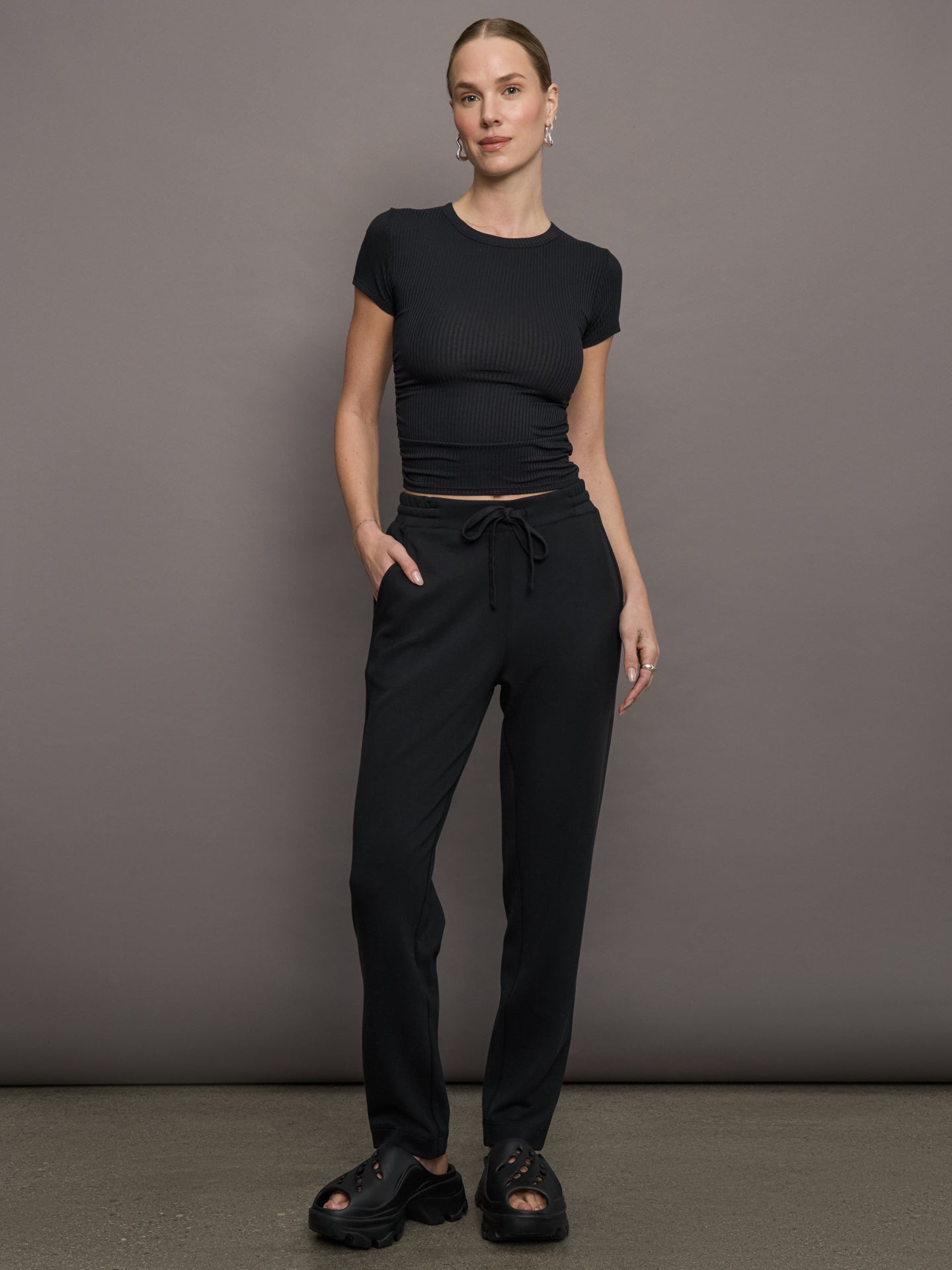 Model wears a short sleeved, ribbed jersey fitted black top with ruching down both sides. 