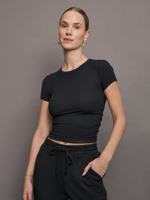 Model wears a short sleeved, ribbed jersey fitted black top with ruching down both sides. 