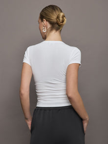 Model wears a short sleeved, ribbed jersey fitted white top with ruching down both sides. 