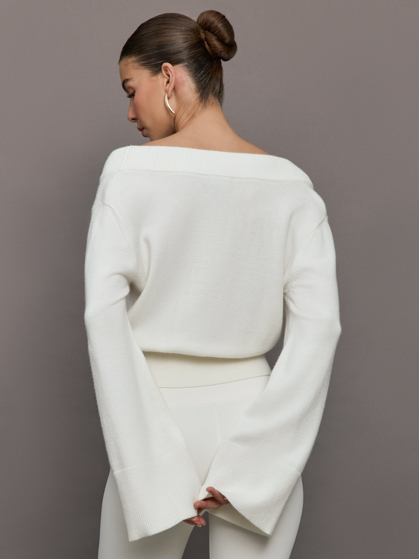 Model wears a white v neck bell sleeved sweater. 