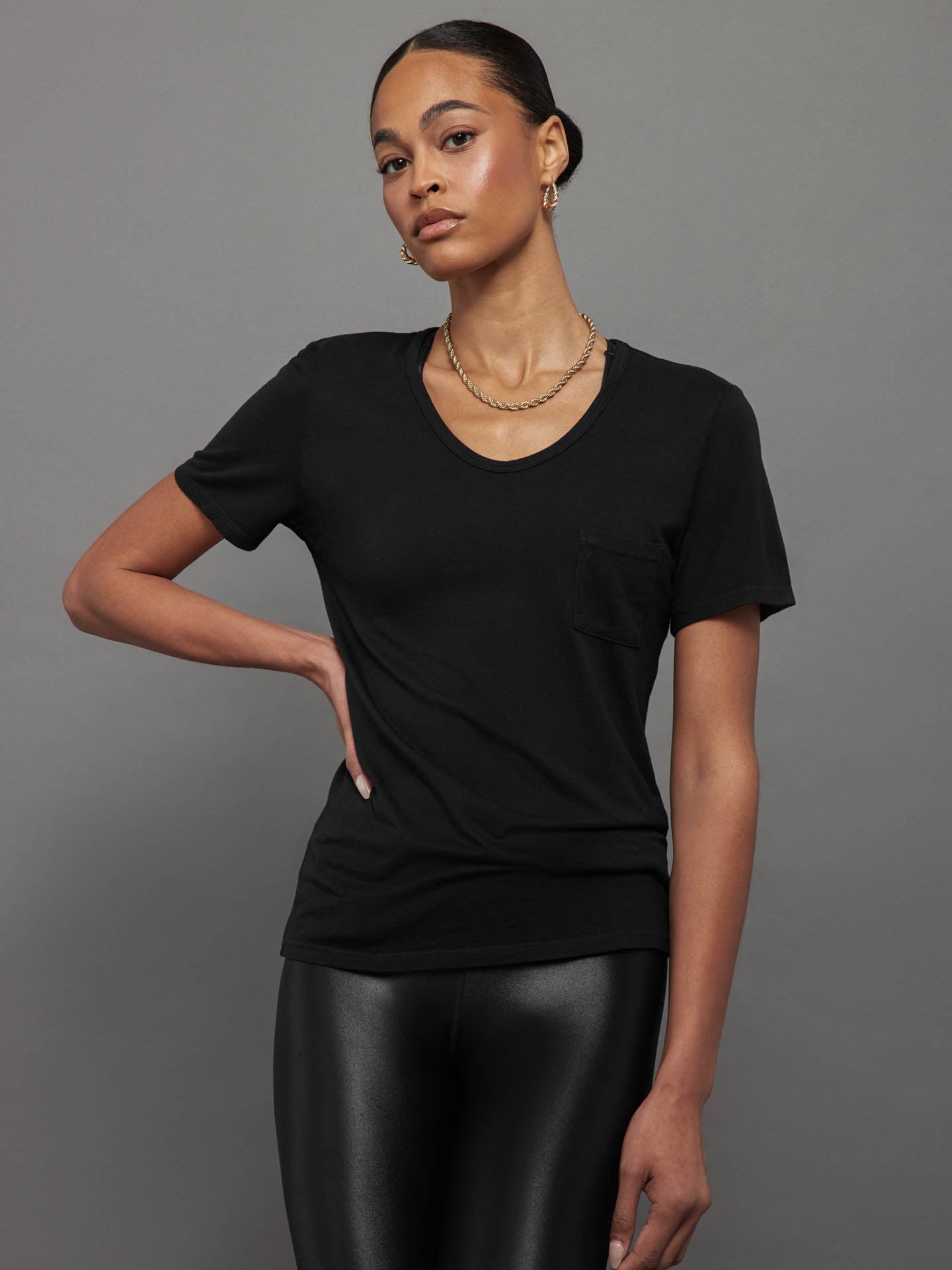 Model wears a black, short sleeve crewneck t-shirt with a front pocket and a relaxed, hip-length fit.




