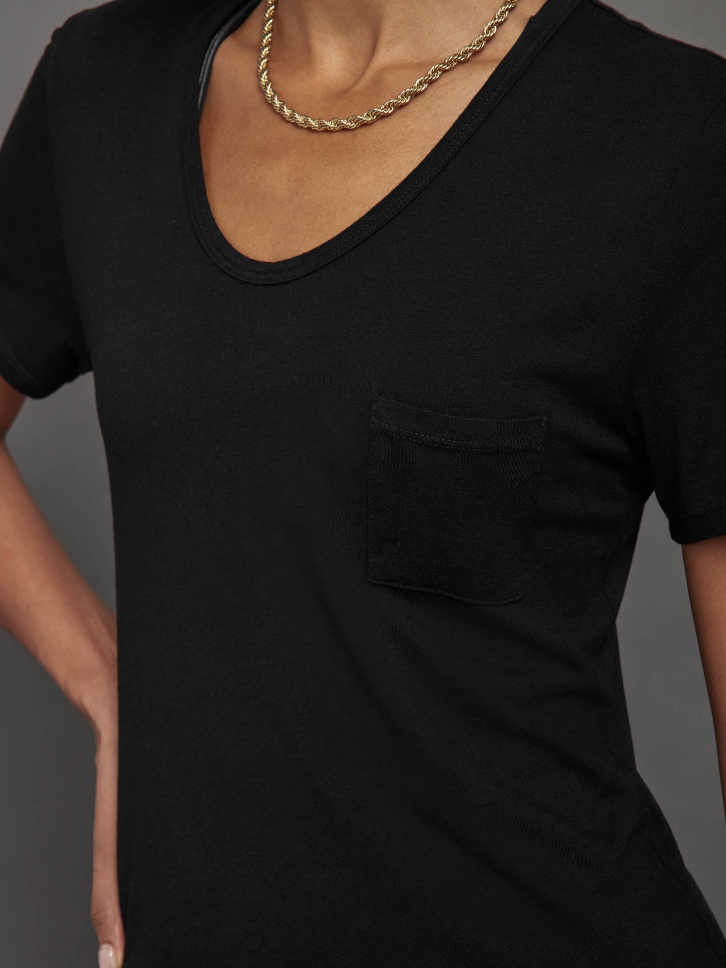 Model wears a black, short sleeve crewneck t-shirt with a front pocket and a relaxed, hip-length fit.

