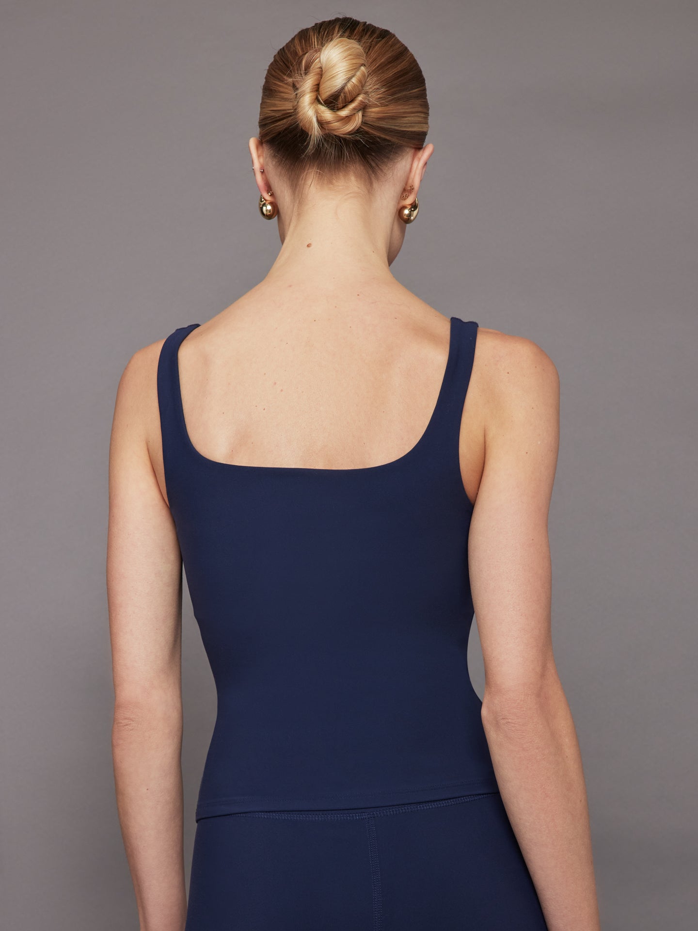 Model wears a navy blue fitted tank top with a wide scoop neckline and a smooth, streamlined look.
