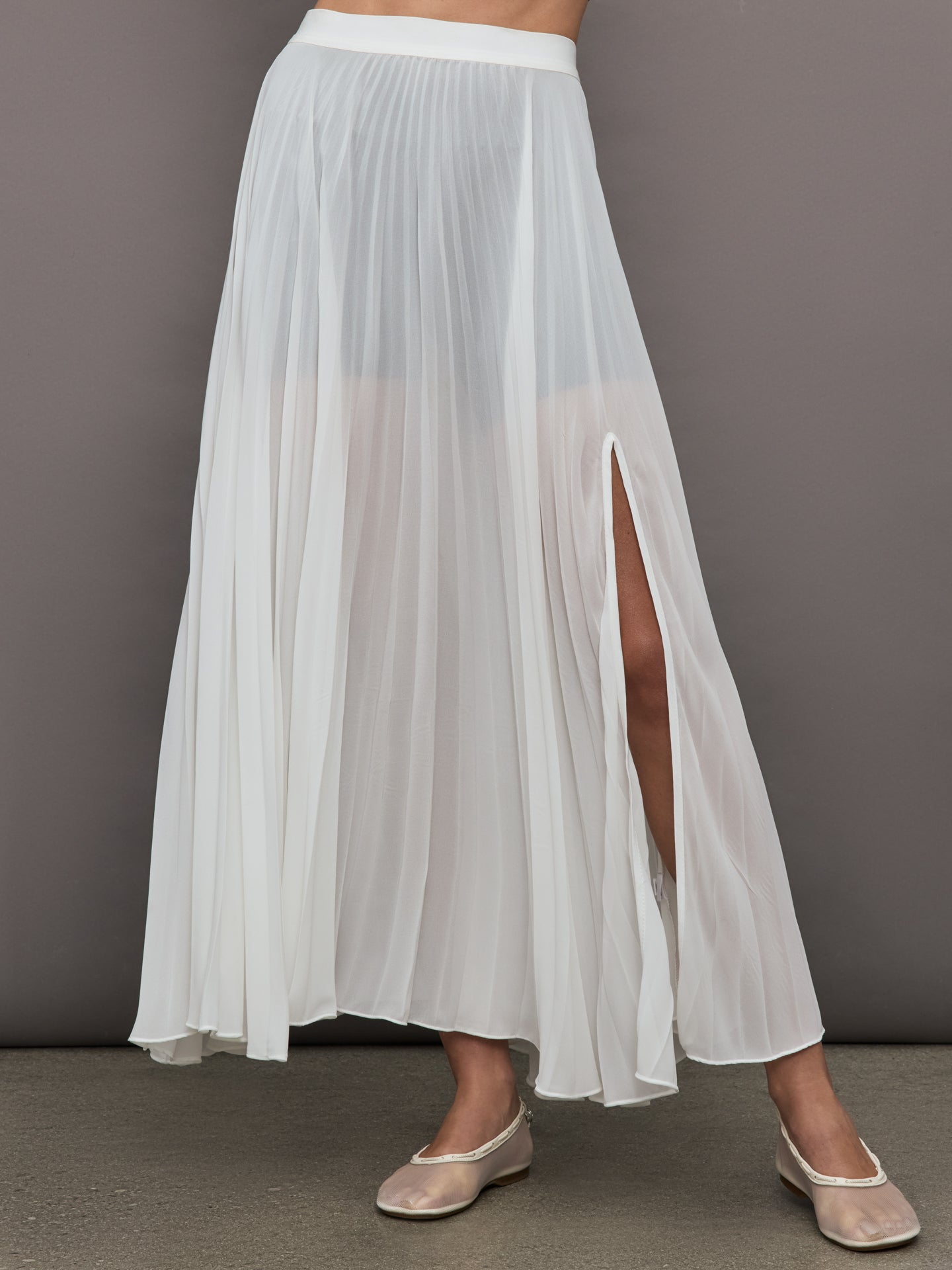 Front view of model wearing Mesh Pleated Skirt Ivory with side slit detail.